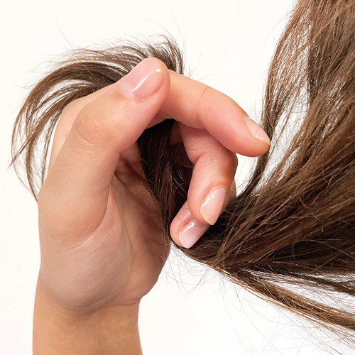 Ragazza con una ciocca di capelli in mano. Punte rovinate, visibilmente Capelli Secchi.