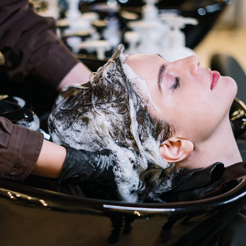 Ragazza al lavaggio mentre la parrucchiera le sta facendo uno shampoo per detergere nel modo corretto i capelli sporchi.