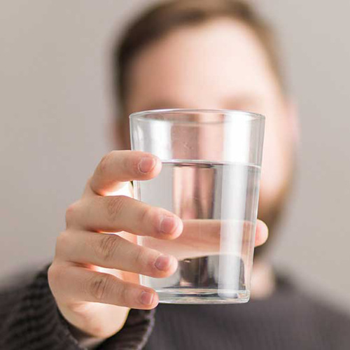 Un ragazzo che tiene in mano un bicchiere di acqua per idratarsi in modo da ottenere capelli sani.