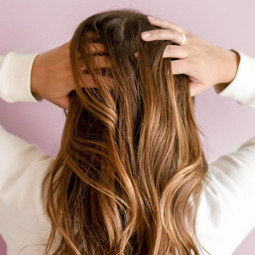 Ragazza di spalle con le mani tra i capelli che si gratta