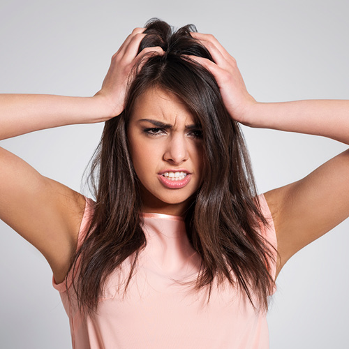 Ragazza mora che si mette le mani in testa perchè sente prurito. La faccia è molto sofferente