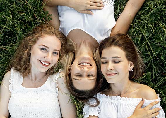 Immagine di tre ragazze sdraite nell'erba che sorridono.