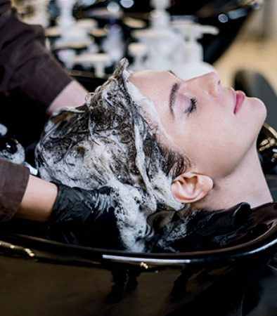 Ragazza al lavaggio mentre la parrucchiera le sta facendo uno shampoo per detergere nel modo corretto i capelli sporchi.